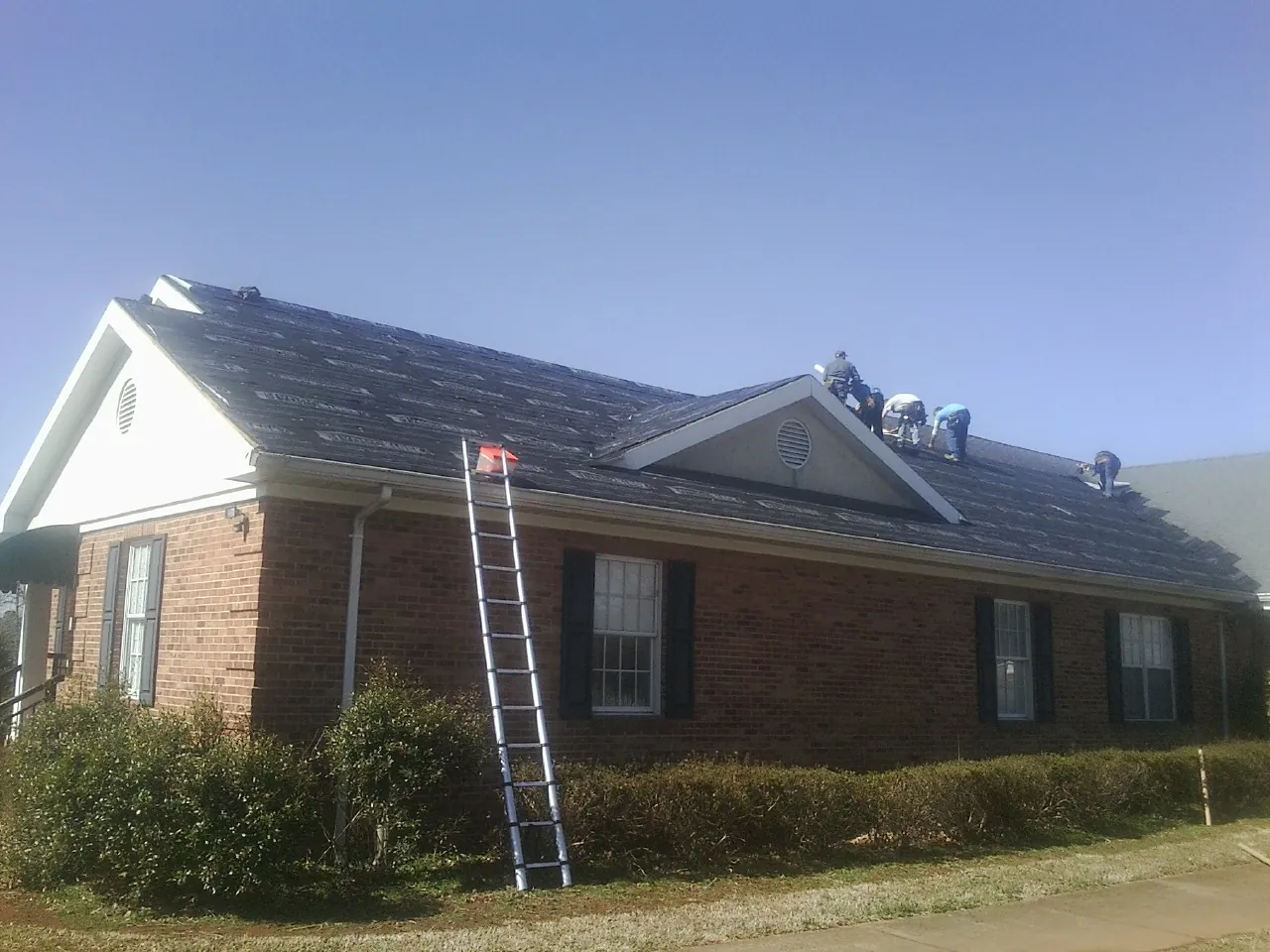 Crew tearing shingles off a brick ranch roof with a ladder set — Metal Roof Repair work by our crew in Port Penn