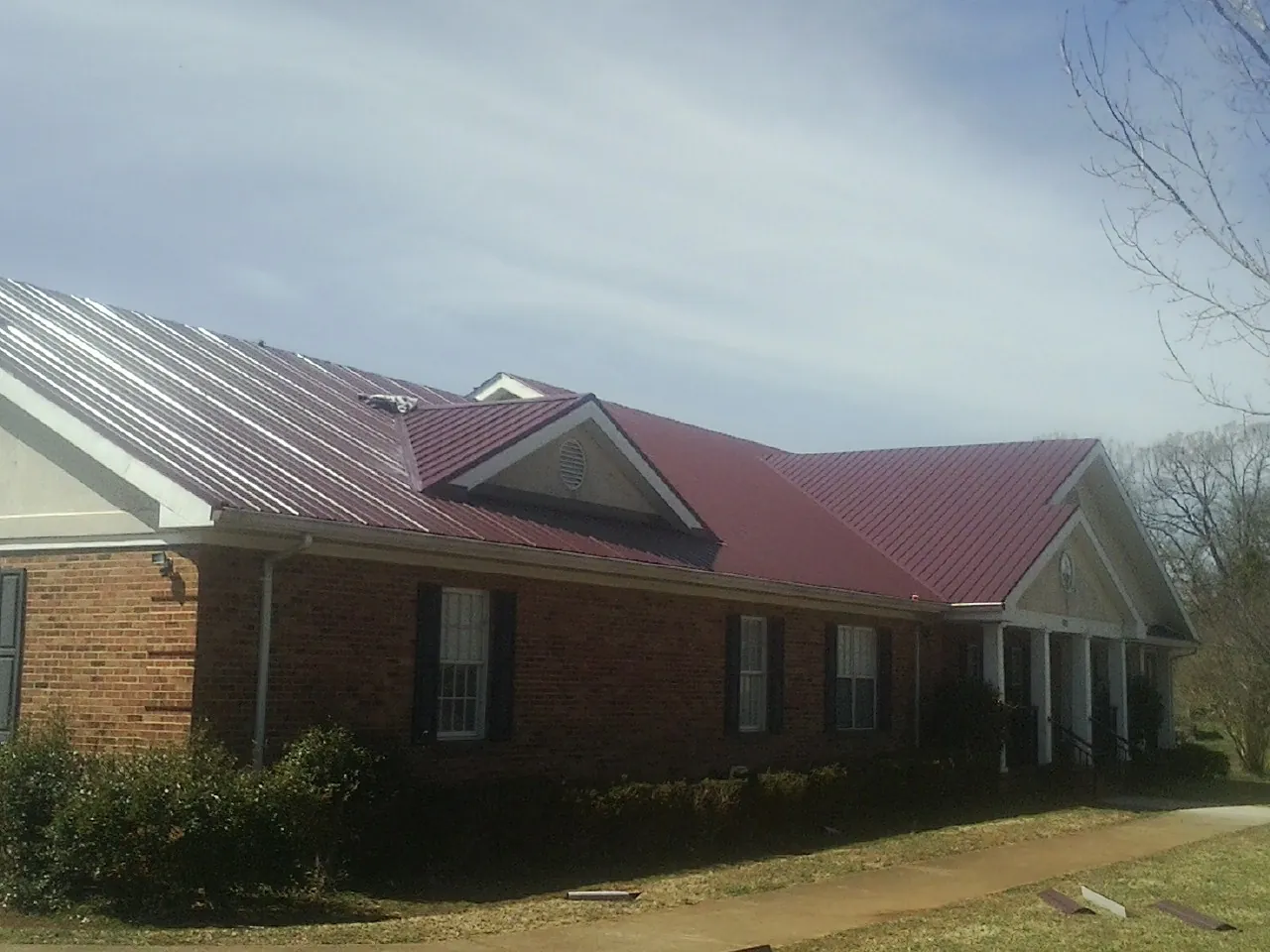 Red metal roof with gabled entries on a long brick building, from a Hail Damage Roof Repair job in Port Penn