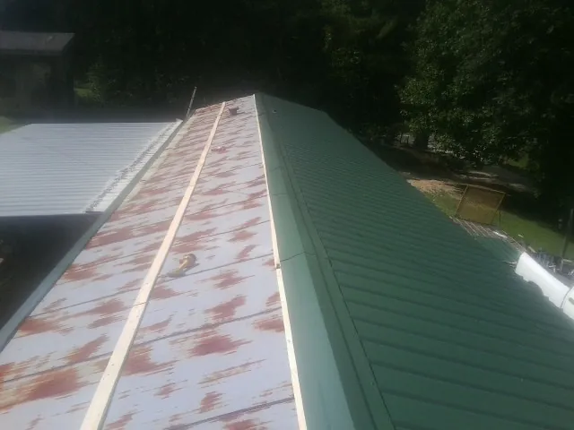 Old rusted panels beside newly installed green metal roofing — Wind Damage Roof Repair by Roofing Brothers in Port Penn