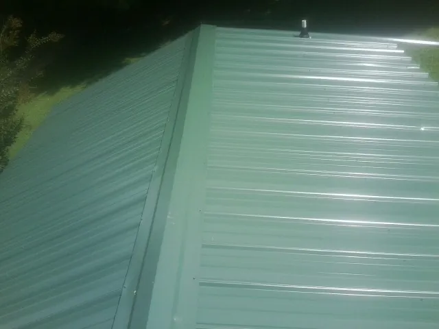 New green metal panels meeting at the ridge of a roof — Flat Roof Repair work by our crew in Port Penn
