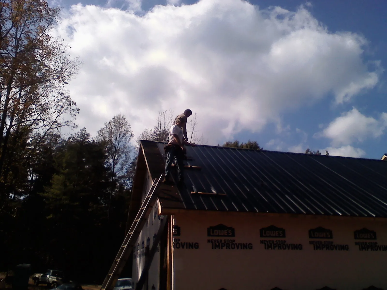 Roofer fastening dark metal panels high against a cloudy sky, from a Roof Inspection job in Port Penn