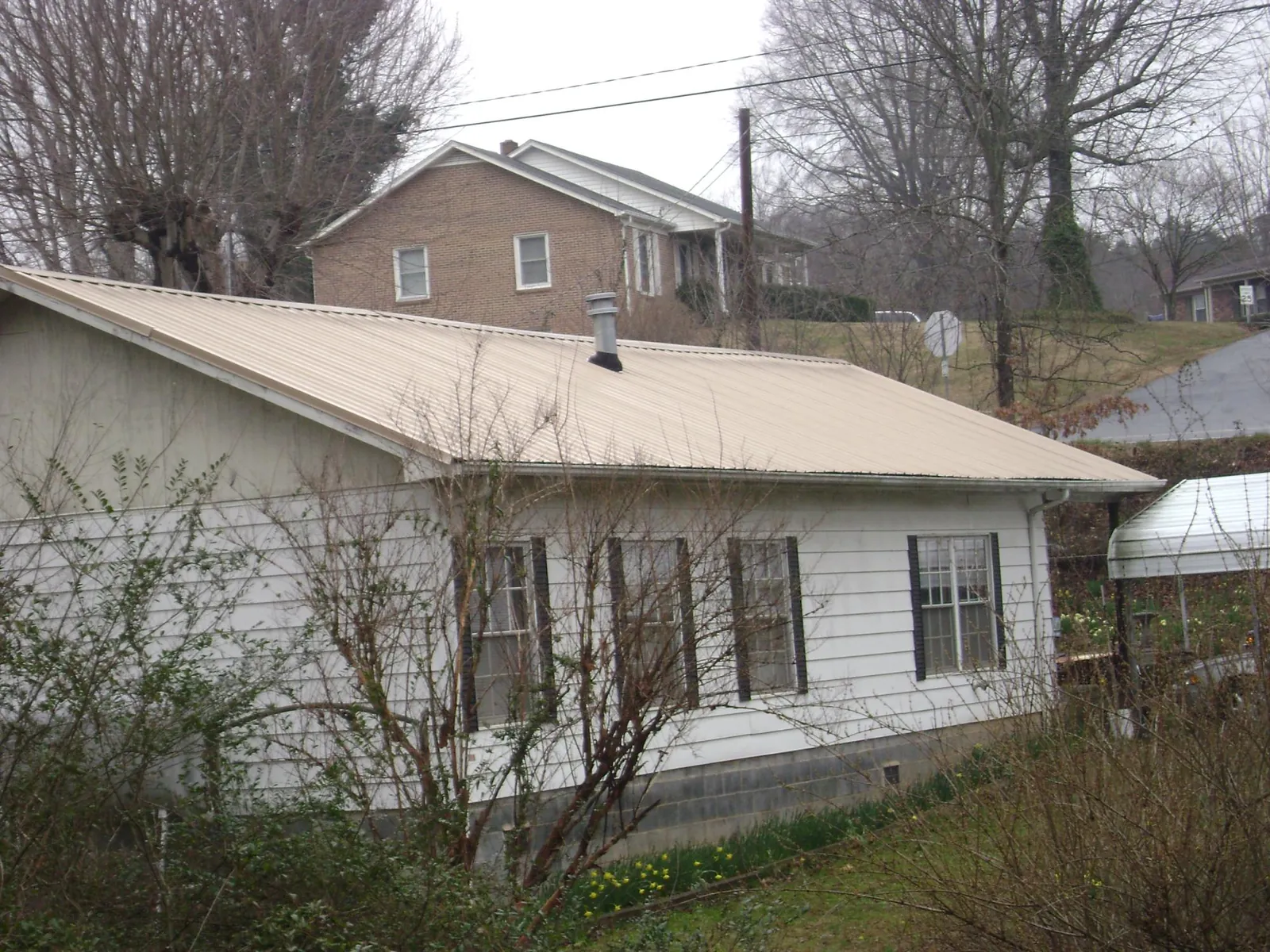 Tan metal roof on a white sided house set into a hillside — Commercial Roofing by Roofing Brothers in Port Penn